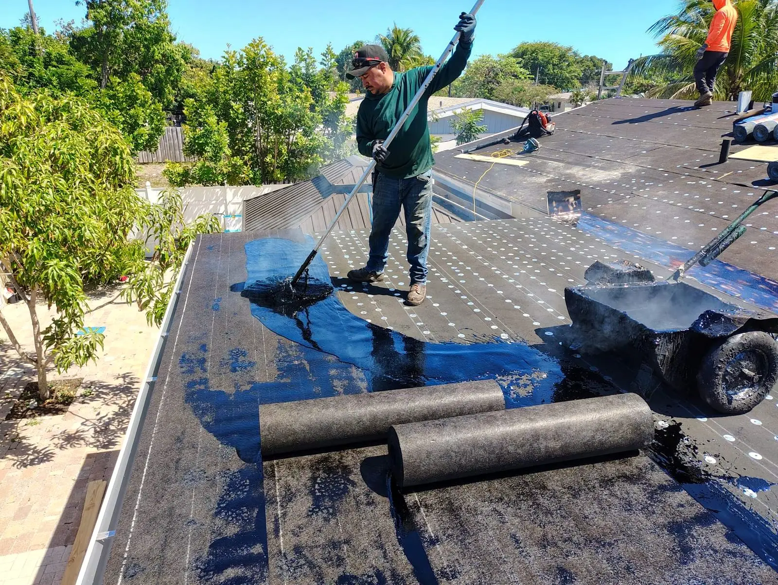 Roofer mopping hot asphalt over a flat roof as new felt is rolled out