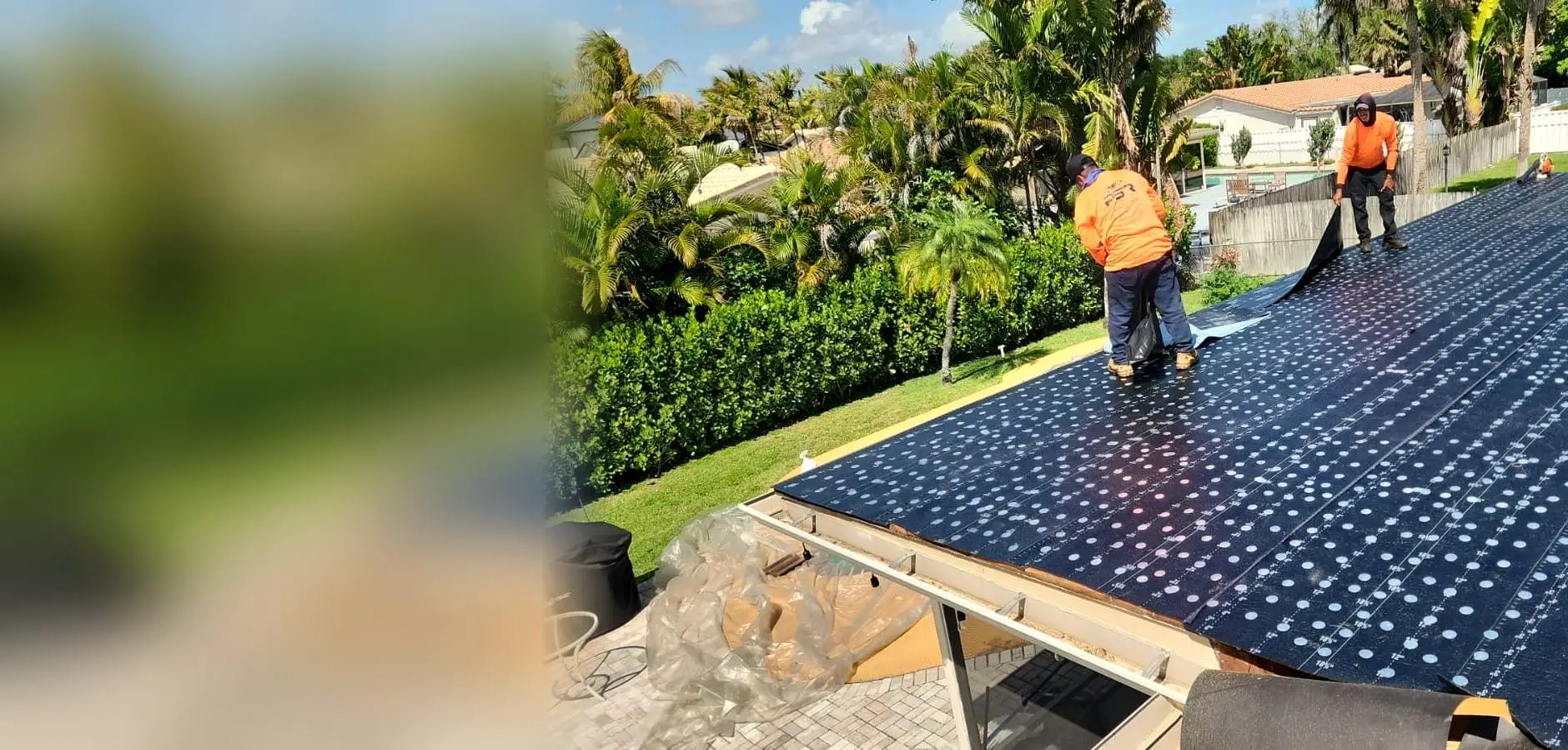 Two PSR crew members in orange shirts rolling out underlayment on a roof, with palm trees behind