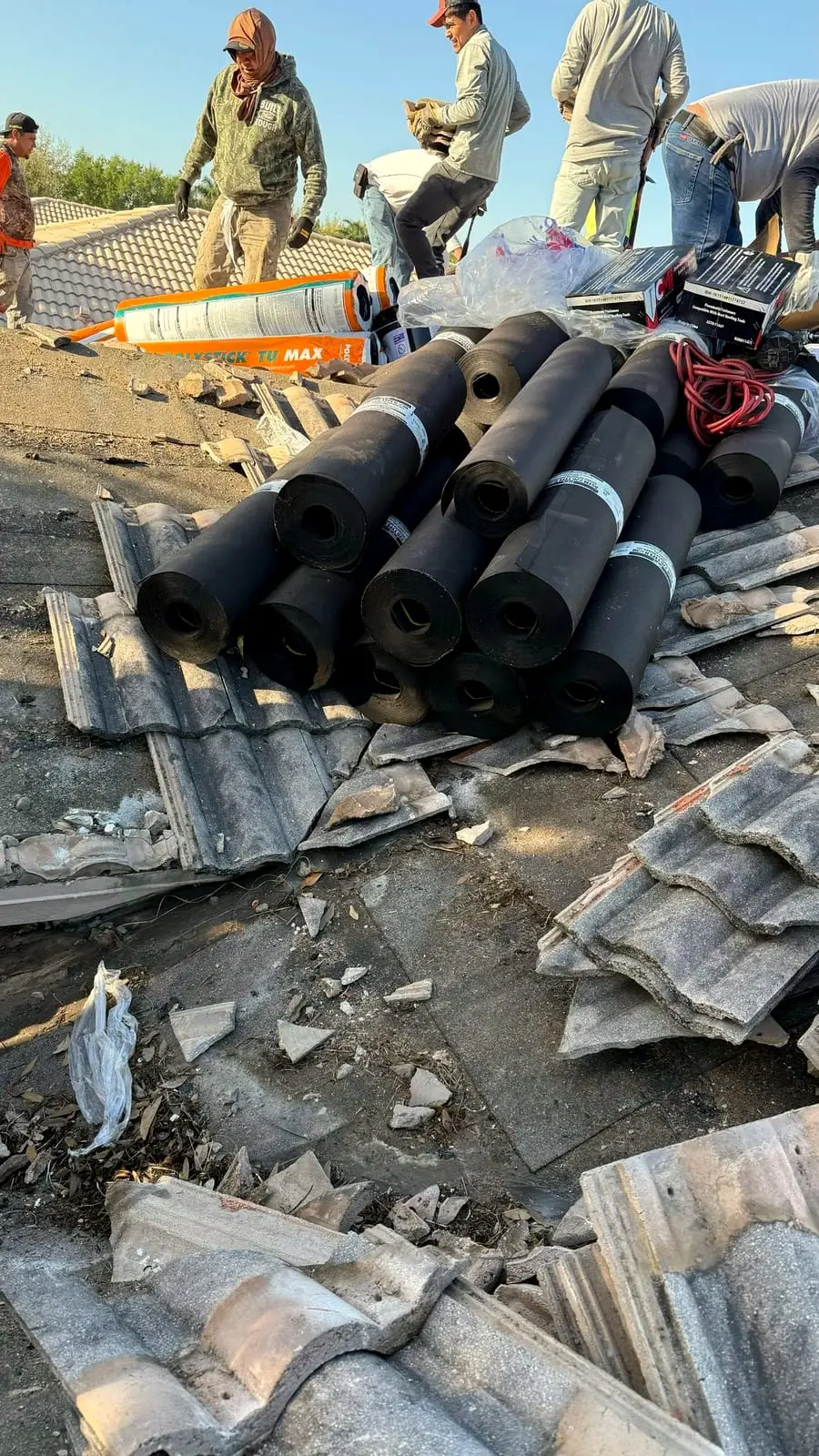 Worn concrete barrel tile coming off a roof, with rolls of new underlayment staged on the deck